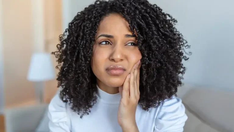 Woman sitting at home with hand on cheek indicating tooth pain